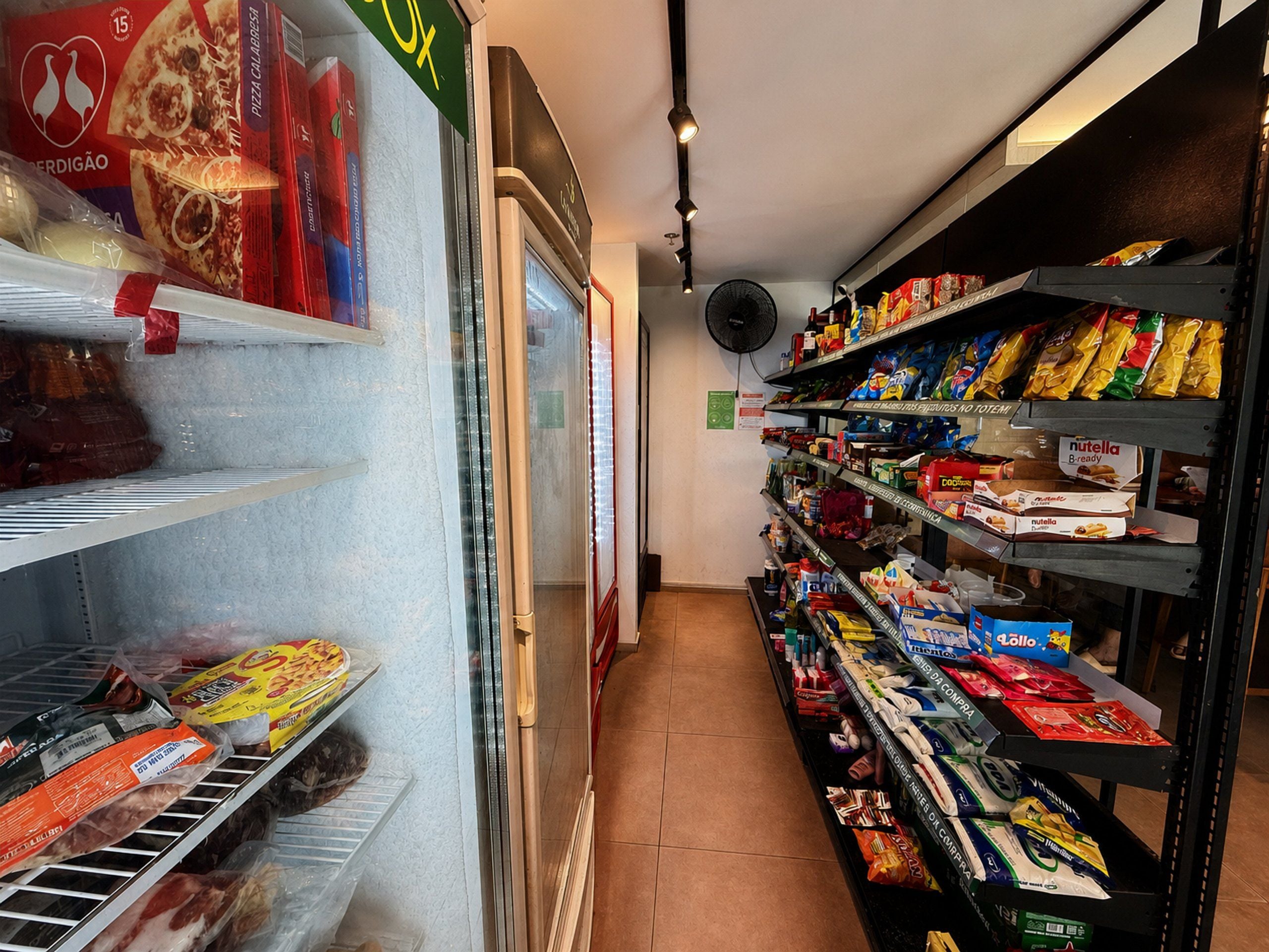 Un pasillo de un supermercado con estantes llenos de diversos productos alimenticios y un congelador a la izquierda.