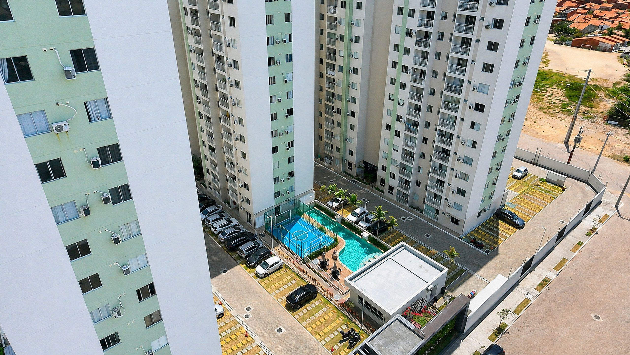 Un edificio residencial alto con varios balcones, una piscina y un estacionamiento.