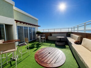 An outdoor patio with a round wooden table, seating area, and a view of the sea. - Hosts BR - Apto no Mirante Clube (Fortaleza)