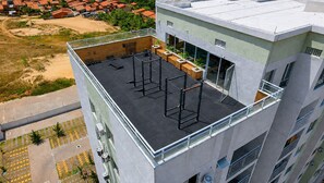 Eine Dachterrasse mit Fitnessgeräten im Freien, einem überdachten Sitzbereich und Blick auf die umliegenden Gebäude.