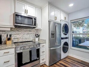 A modern kitchen with white cabinets, stainless steel appliances, a microwave, oven, refrigerator, and a built-in washer and dryer.