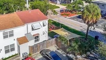 Et boligområde med et hvidt hus, en rød bil og en sort bil parkeret på indkørslen.