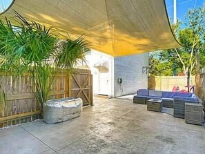An outdoor patio area with a shaded seating arrangement, a potted plant, and a wooden fence.