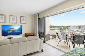 A balcony with a view of a marina, a flat-screen TV, a sofa, and a dining table with chairs. - Ilikai Hotel & Luxury Suites | 2 Marina View Condos Sleeps 10 | Car Incl. w/ 6+Nights | ML-4247 by KBM (Honolulu)