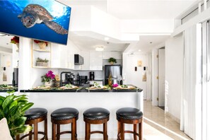 A modern kitchen with white cabinets, a large island with stools, a flat-screen TV, and a potted plant. - Ilikai Hotel & Luxury Suites | 2 Marina View Condos Sleeps 10 | Car Incl. w/ 6+Nights | ML-4247 by KBM (Honolulu)