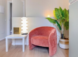Ein Zimmer mit weißem Tisch, rotem Stuhl, einer Lampe und einem Topfpflanzen.