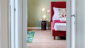 A bedroom with a bed, a bedside table with a mirror, and a green patterned rug. - Flatsharing - Gioia Coral suite - 1 bedroom (Milan)