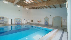 A large indoor swimming pool with clear blue water, wooden beams on the ceiling, and dolphin murals on the walls. - Apartment '6-person' with Shared Pool, Wi-Fi and Air Conditioning (Portimão)