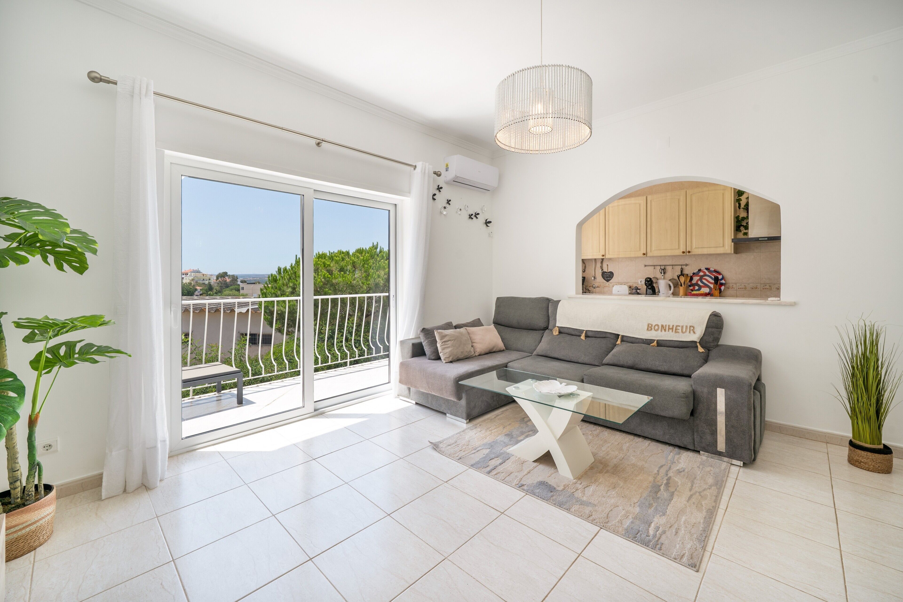 Una sala moderna con un sofá gris, una mesa de centro de vidrio y vistas a un balcón exterior a través de puertas correderas.