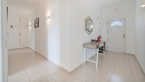 A hallway with a tiled floor, a white door, a wall-mounted mirror, and a small table with a fire extinguisher. - Apartment '6-person' with Shared Pool, Wi-Fi and Air Conditioning (Portimão)