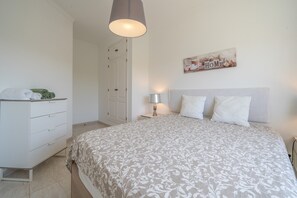 Un dormitorio con cama, cómoda, mesita de noche, lámpara y puerta.