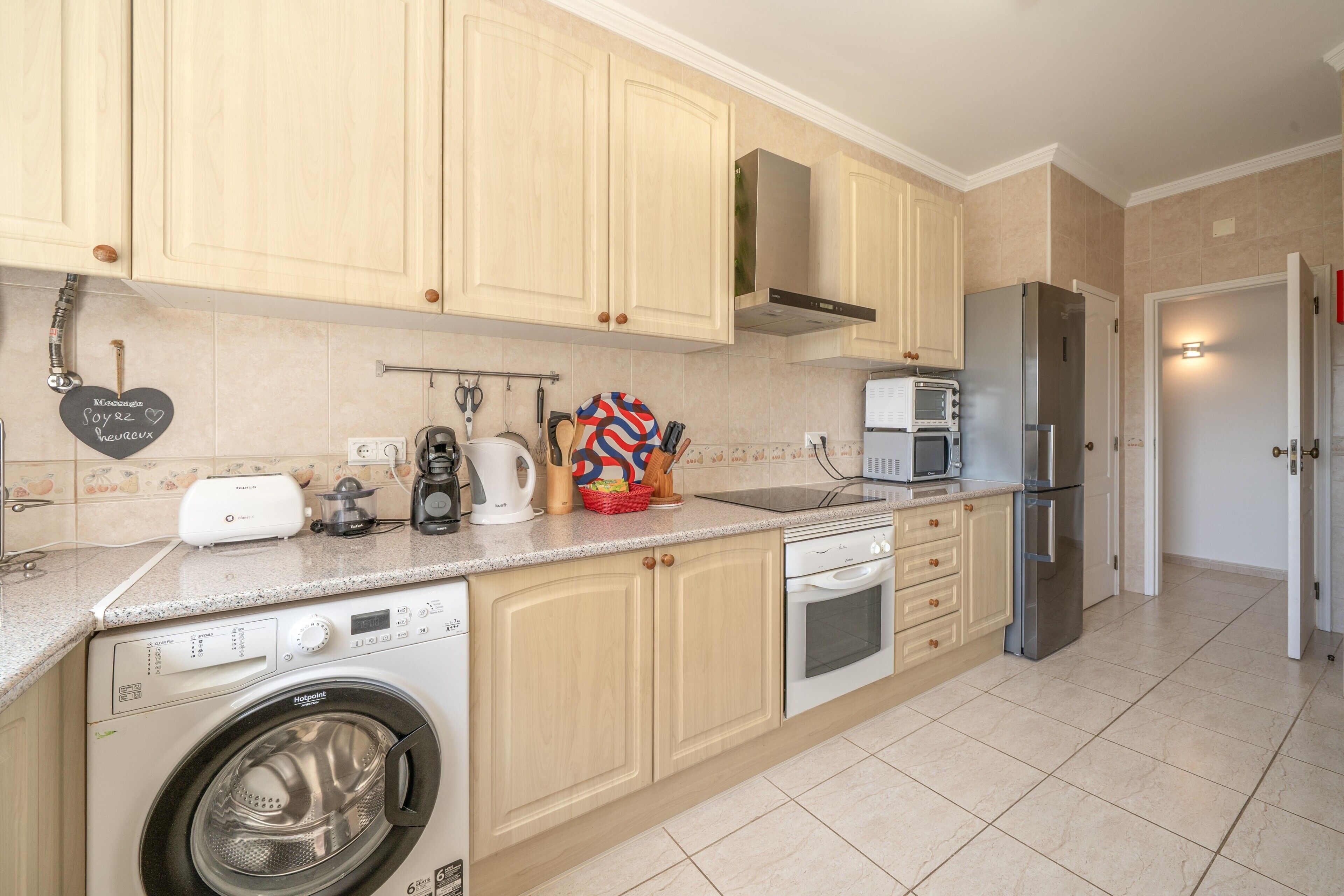 Una cocina moderna con armarios de madera, lavadora integrada, refrigerador de acero inoxidable y microondas.