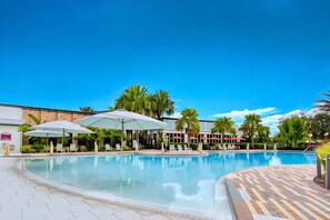 A swimming pool with lounge chairs and umbrellas, surrounded by palm trees and a brick building. - Disney Home w Lake View BBQ Patio & Resort Access (Davenport)