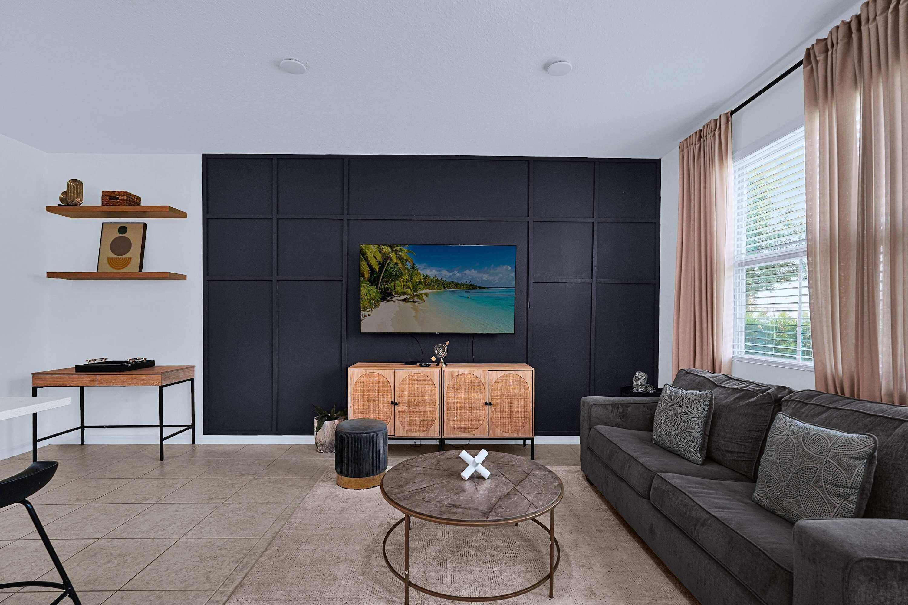 A modern living room with a dark wall panel, a wooden cabinet, a grey sofa, a round coffee table, and a television mounted on the wall.