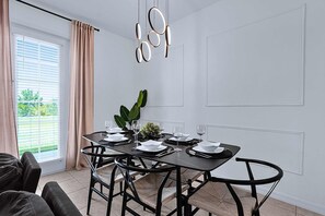 A dining area with a table set for four, black chairs, a modern pendant light, and a window with curtains. - Disney Home w Lake View BBQ Patio & Resort Access (Davenport)