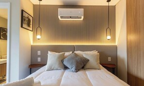 Ein Hotelzimmer mit einem Bett, zwei Nachttischen, einer Wand-Klimaanlage und zwei Wandleuchten.