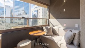A modern room with a sofa, a small round table, and a view of the cityscape through large windows. - New Studio 650 m From Paulista Avenue Hmj0517 (São Paulo)