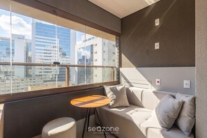 Ein modernes Zimmer mit einer Couch, einem kleinen runden Tisch und Blick auf die Stadt durch große Fenster.