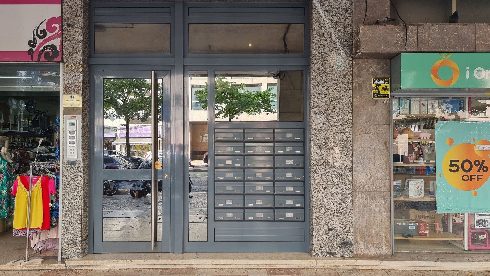 A storefront with a grey metal door, a display of colorful clothing outside, and a sign indicating a 50% discount.