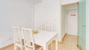 Une table à manger blanche avec quatre chaises, un petit set de table en fibres tressées et une porte avec une pancarte rouge.