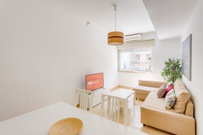 Un salon moderne comprenant un canapé, un téléviseur, une table à manger et un luminaire suspendu.