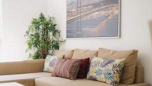 Un canapé beige agrémenté de coussins à motifs, une plante en pot et un tableau encadré représentant un pont.