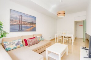 Un salon moderne avec un canapé, une table basse et un coin repas avec des chaises. Un grand tableau encadré représentant un pont est accroché au mur.