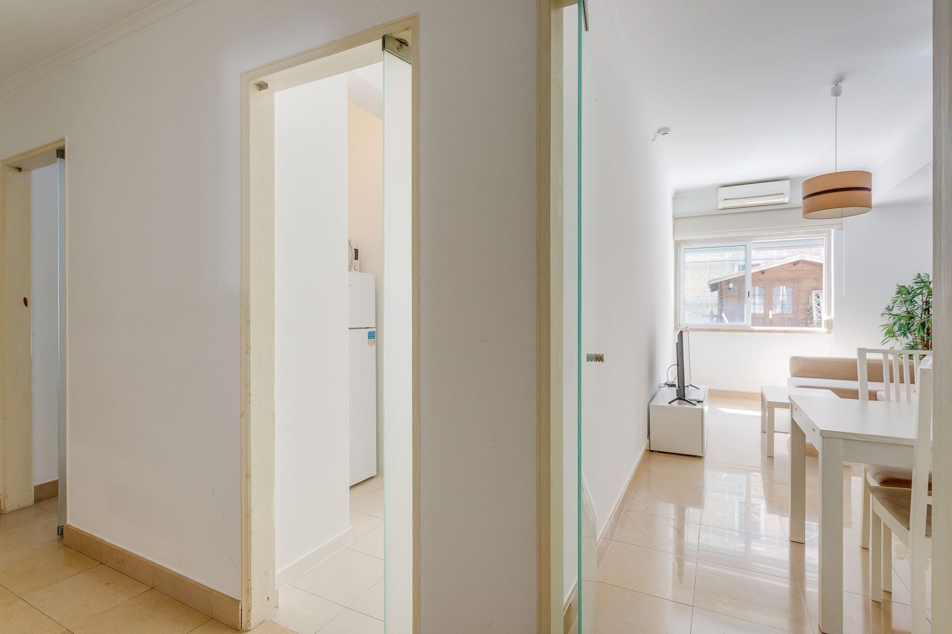 Um interior moderno com um corredor que leva a uma sala de jantar, uma geladeira e uma janela com vista.