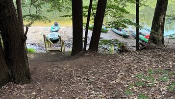 A forested area with a river, kayaks, and a paddleboard.