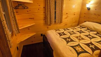 A wooden cabin room with a bed, a hanging light, and a window with curtains.