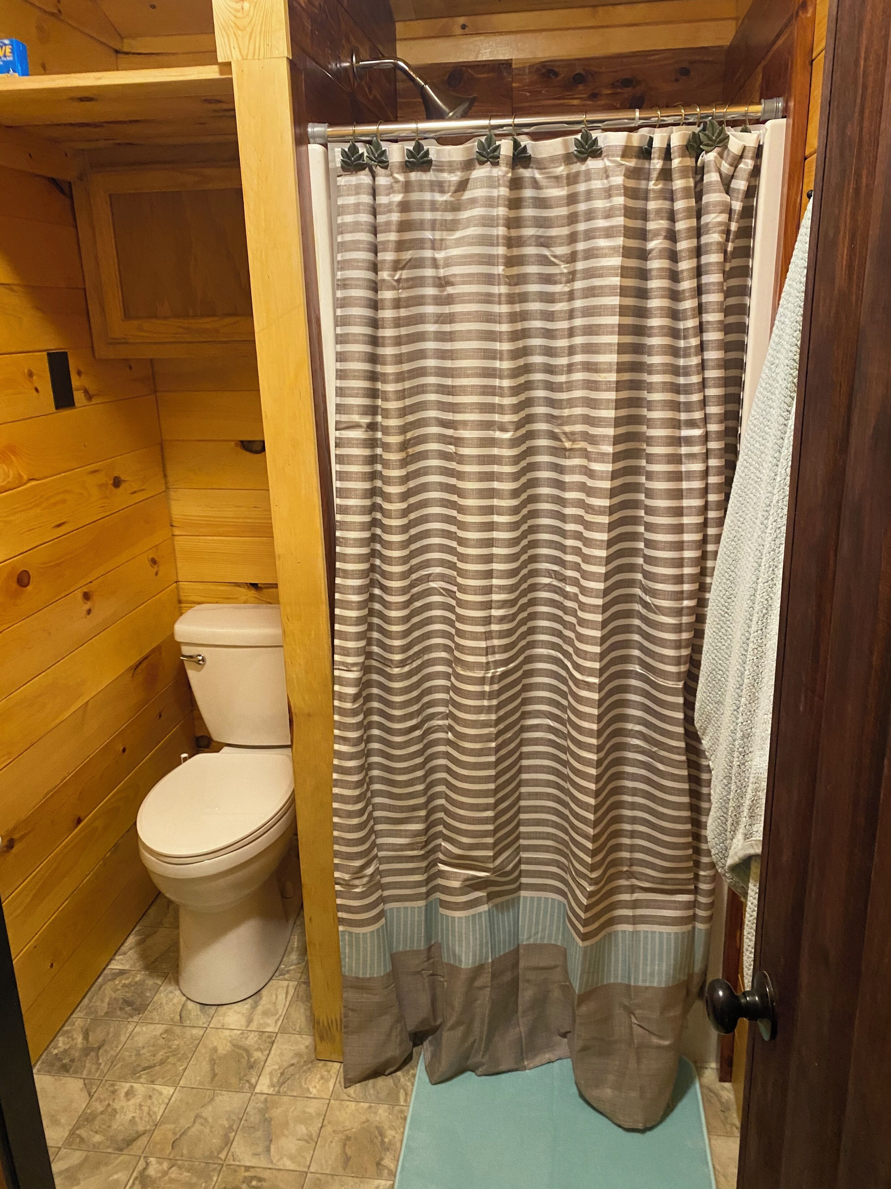 Un baño de madera con cortina de ducha a rayas, un inodoro y un perchero para toallas.
