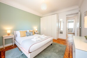 Ein Hotelzimmer mit Bett, Nachttischen, einem Spiegel und einem sichtbaren Badezimmer hinter einer offenen Tür, sowie einem grünen Teppich.