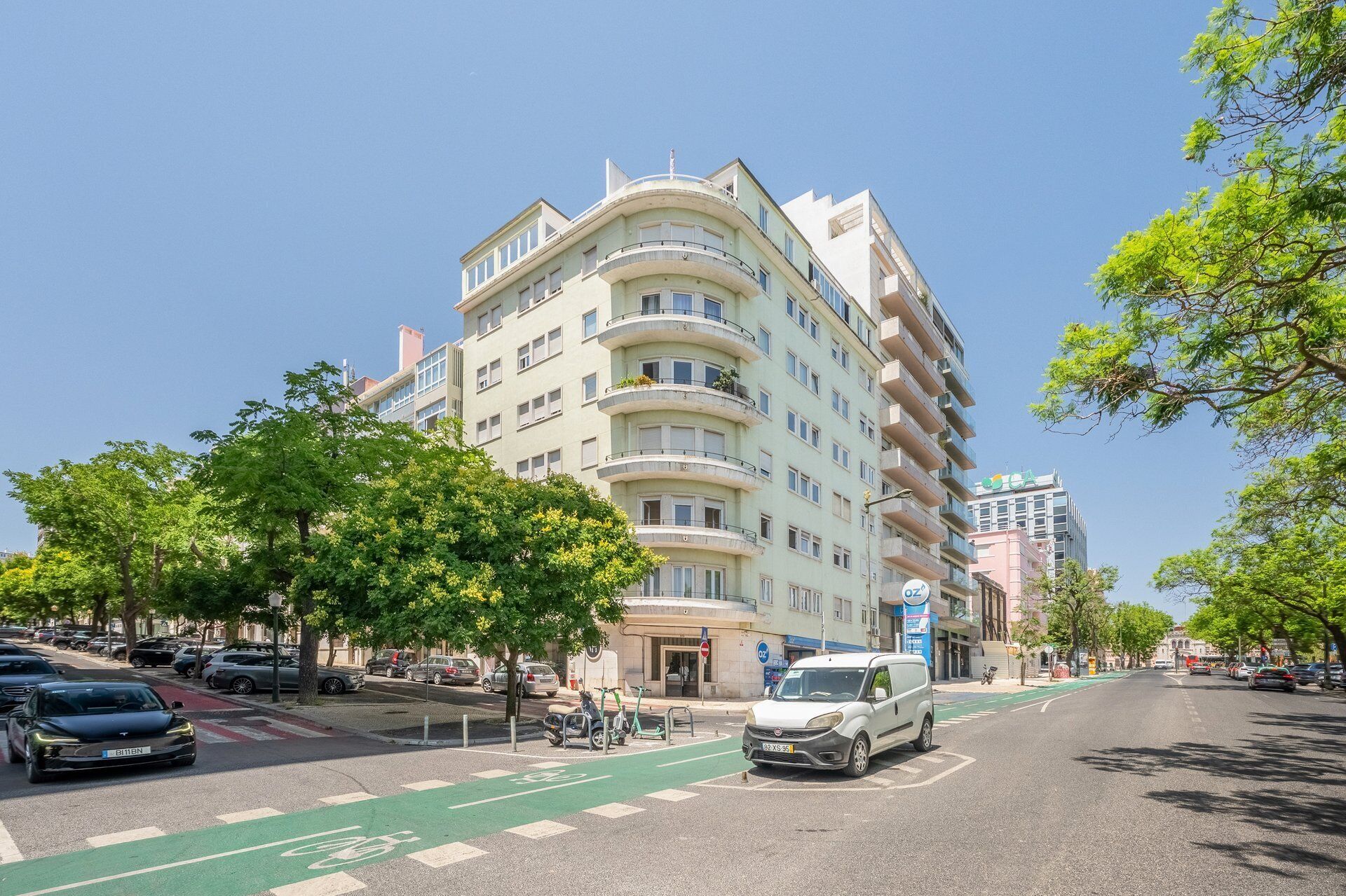 Un immeuble à plusieurs étages doté de balcons, d’une piste cyclable verte et de voitures garées.
