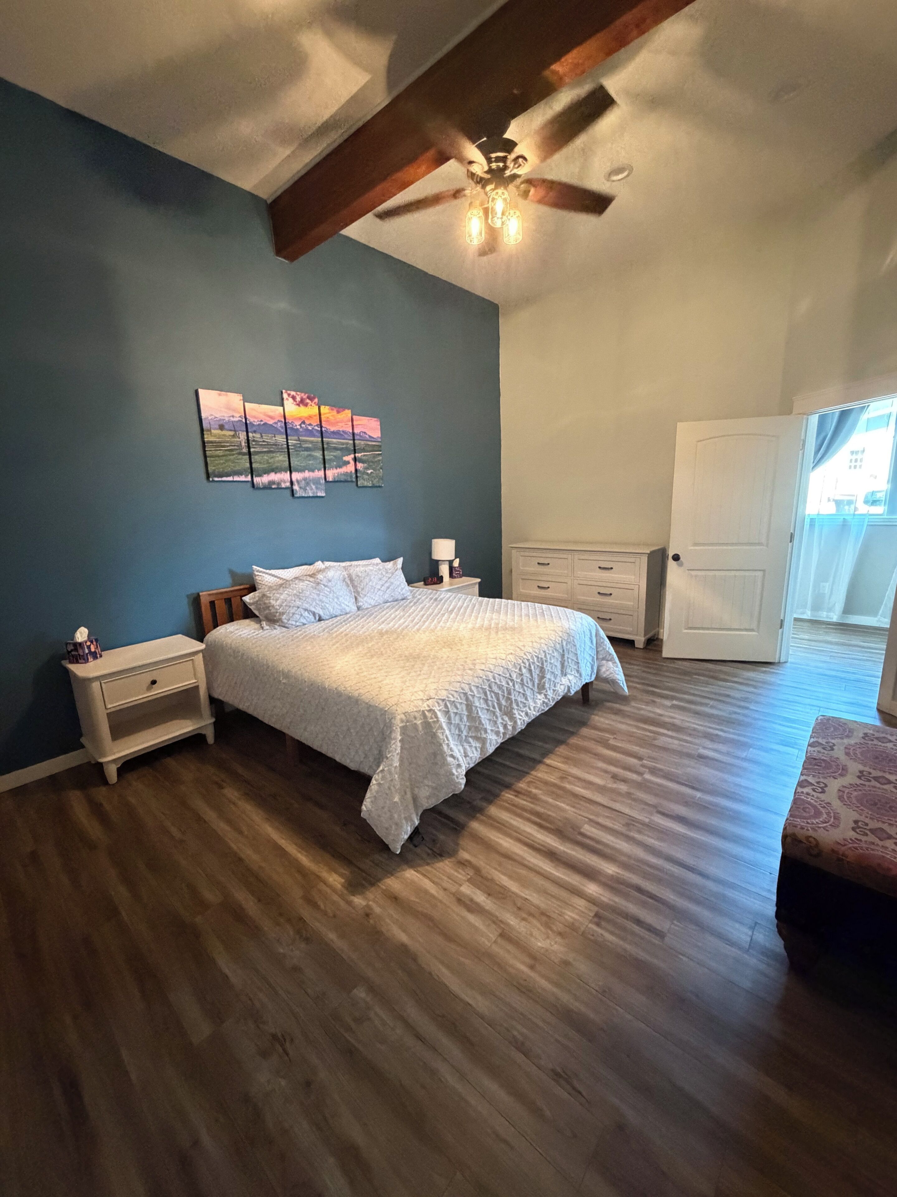 A bedroom with a bed, nightstands, a ceiling fan, and a door.