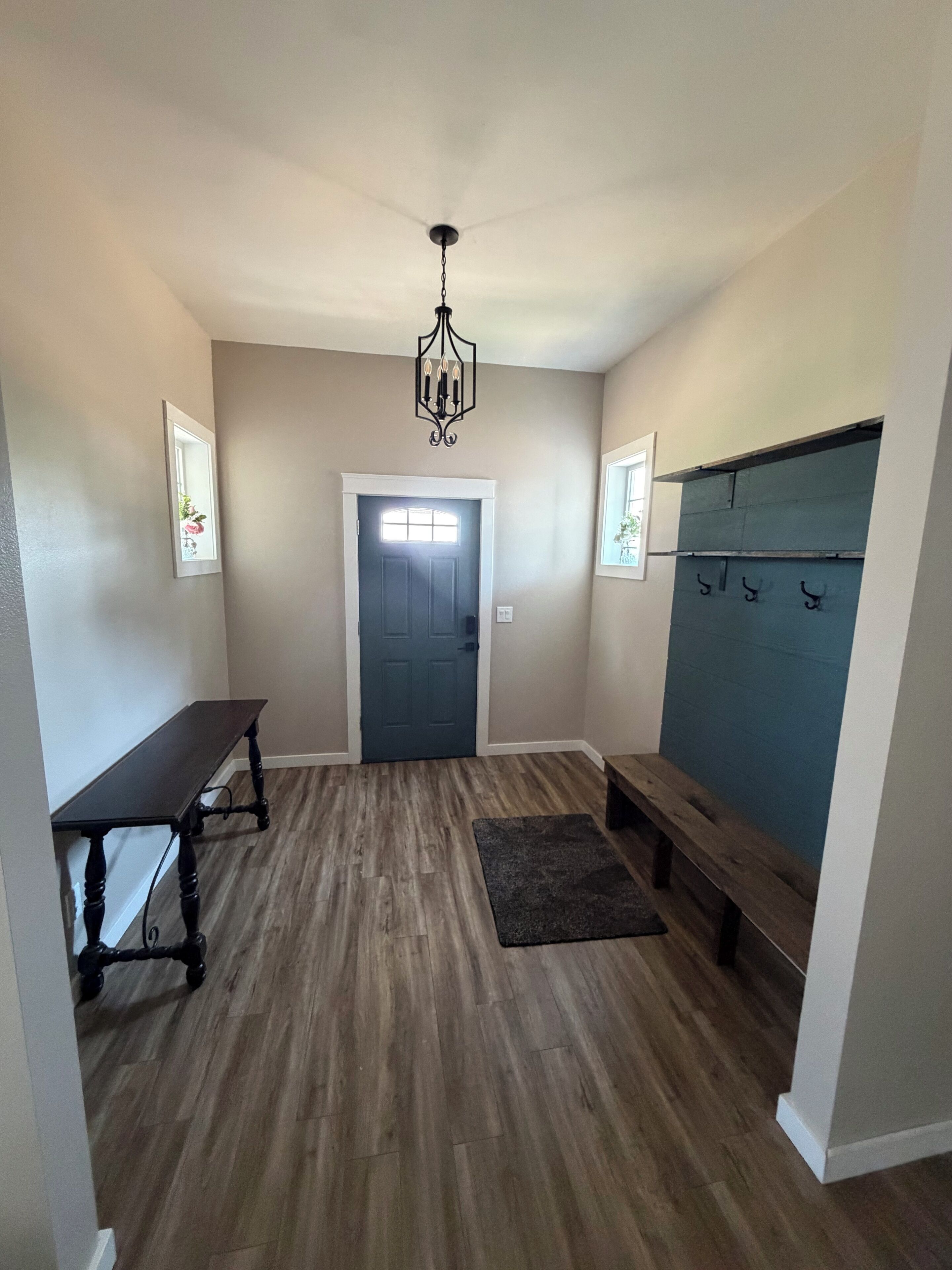 A hallway with a dark wooden bench, a small table, a chandelier, a door, and a coat rack.