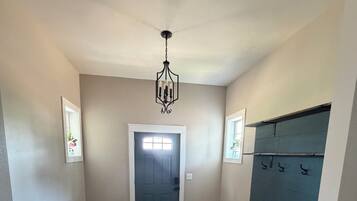 A hallway with a dark wooden bench, a small table, a chandelier, a door, and a coat rack.