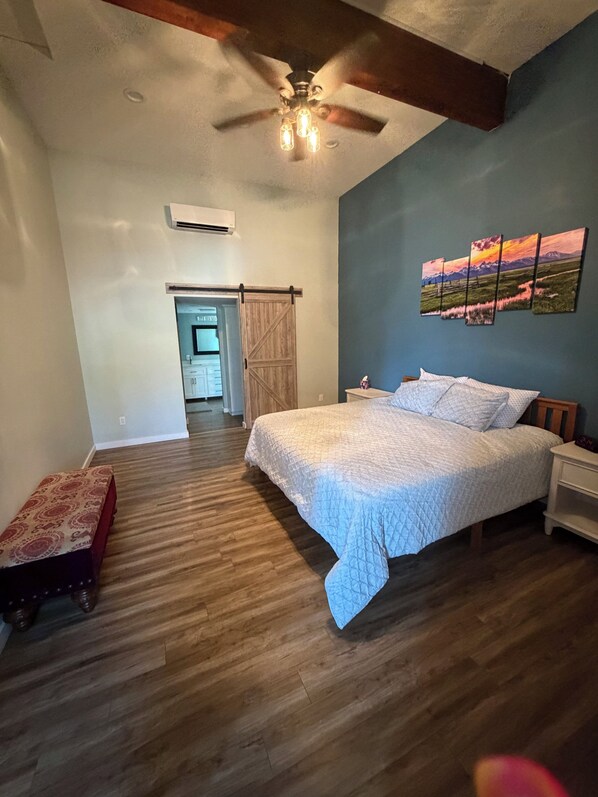 A bedroom with a bed, a nightstand, a wall-mounted painting, a ceiling fan, and a sliding barn-style door.
