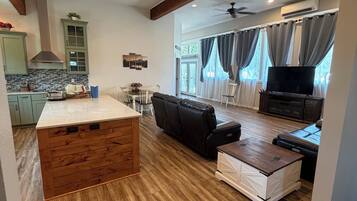 A spacious living area with a wooden floor, a central island, a black leather sofa, and a television.