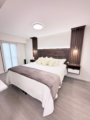 A modern bedroom with a large bed, a bedside table, a nightstand, a ceiling light, and a window with blinds. - Beautiful 3-bedroom apartment in delightful Miraflores neighborhood (Miraflores)