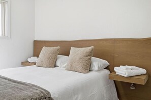 A neatly made bed with white linens, two fluffy pillows, and a wooden headboard.