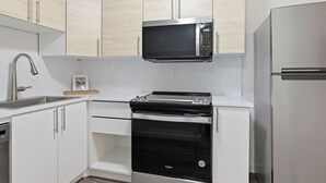 Eine Küche mit weißen Schränken, einer Edelstahl-Mikrowelle, einem schwarzen Backofen und einem Kühlschrank.
