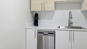 Eine moderne Küche mit weißen Schränken, einem integrierten Geschirrspüler, einer Kaffeemaschine und einem Edelstahl-Spülbecken.