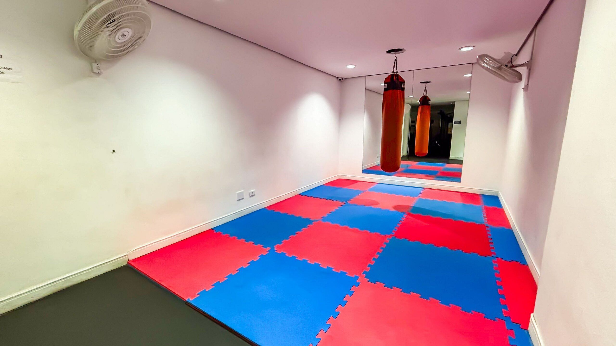 Un pasillo con piso entrelazado en rojo y azul, una pared blanca y un ventilador de techo.