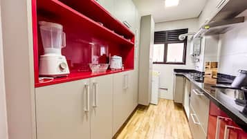 Una cocina con un estante rojo, una licuadora, una olla de cocción lenta y una estufa.