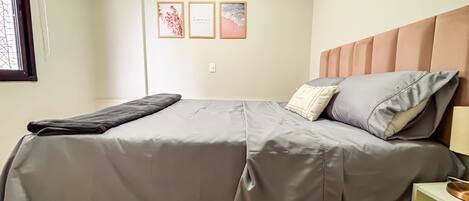 A bed with a grey bedspread, a pillow with a tag, and a bedside table with a lamp.