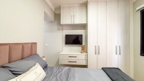 A bedroom with a bed, a TV, a desk, and a wardrobe. - SHB Lazer Completo com sacada (Guarujá)