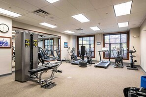Ein Fitnessstudio mit verschiedenen Trainingsgeräten, einer Uhr an der Wand und großen Fenstern.