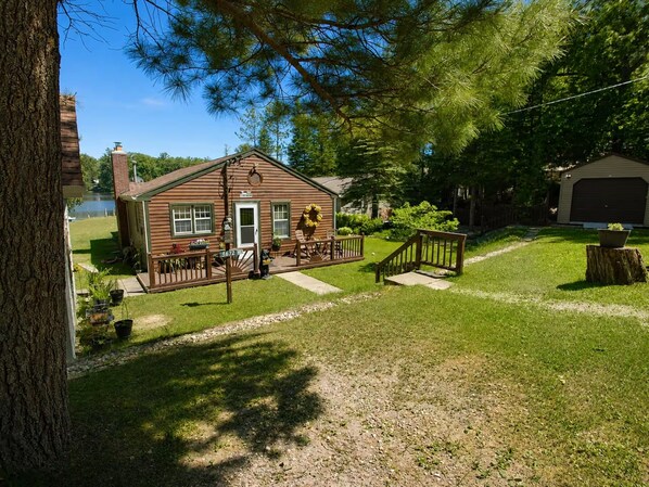 A wooden cabin with a porch, a fenced yard, and a garage.