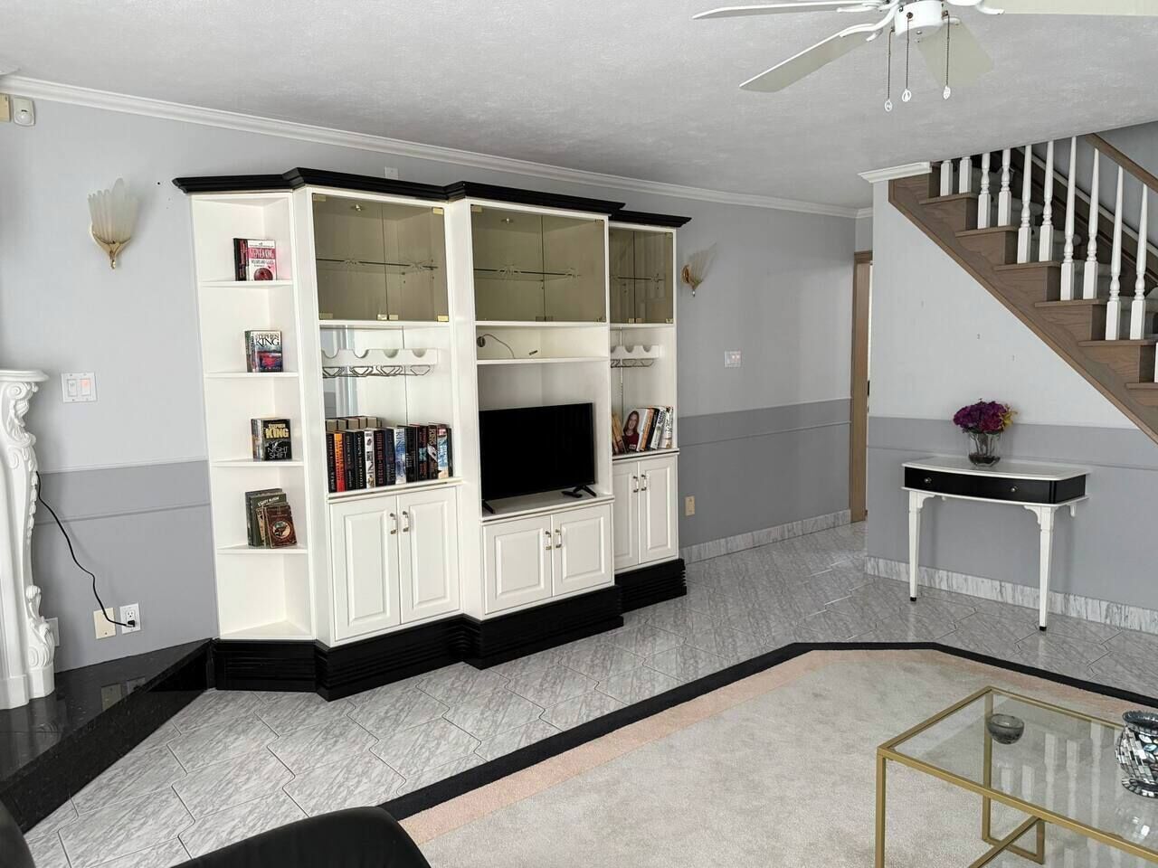 A living room with a white entertainment unit, a glass coffee table, and a staircase.