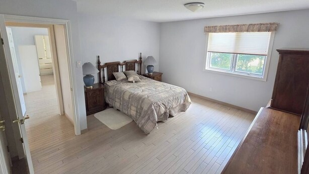A bedroom with a bed, bedside tables, a window with blinds, and a door leading to another room.